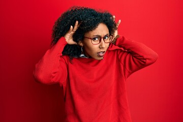 Fototapeta na wymiar Beautiful african american woman with afro hair wearing sweater and glasses trying to hear both hands on ear gesture, curious for gossip. hearing problem, deaf
