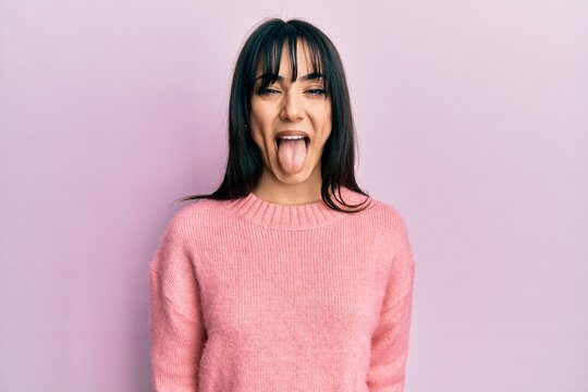 Young brunette woman with bangs wearing casual winter sweater sticking tongue out happy with funny expression. emotion concept.