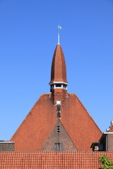 Obraz premium Amsterdam School of Architecture Building Detail with Spire and Red Roof Tiles Against a Blue Sky in Amsterdam, Baarsjes District