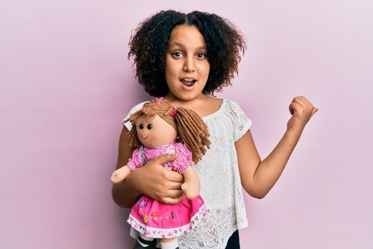 Young little girl with afro hair holding animal doll toy pointing thumb up to the side smiling happy with open mouth