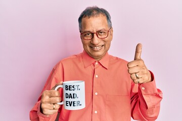 Middle age indian man drinking mug of coffee with best dad ever message smiling happy and positive,...
