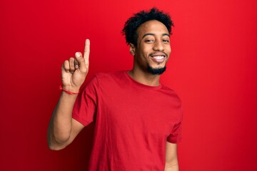 Young african american man with beard wearing casual red t shirt showing and pointing up with...