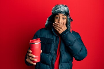 Young african american man with beard wearing winter hat holding hot coffee on thermo covering...
