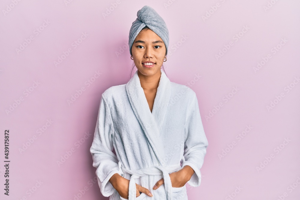 Wall mural Young chinese woman wearing shower towel cap and bathrobe with a happy and cool smile on face. lucky person.