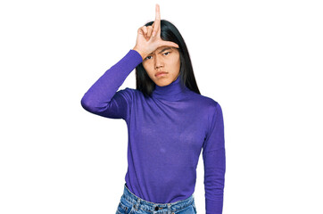 Beautiful young asian woman wearing casual clothes making fun of people with fingers on forehead...