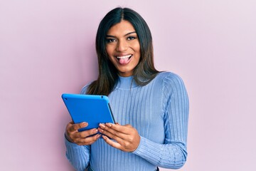 Fototapeta premium Young latin transsexual transgender woman using touchpad device sticking tongue out happy with funny expression.