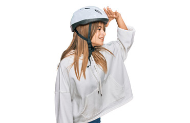 Teenager caucasian girl wearing bike helmet very happy and smiling looking far away with hand over head. searching concept.