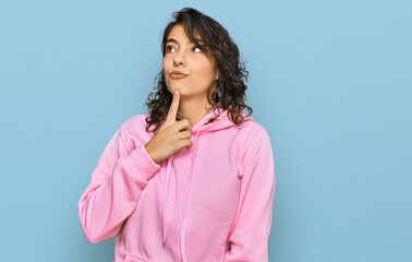 Young hispanic woman wearing casual sweatshirt thinking concentrated about doubt with finger on...