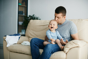 Joyful baby laughing while father is kissing him at home.