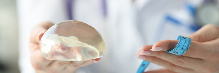 Doctor holding breast implant and measuring tape closeup
