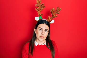 Young hispanic woman wearing cute christmas reindeer horns with serious expression on face. simple...