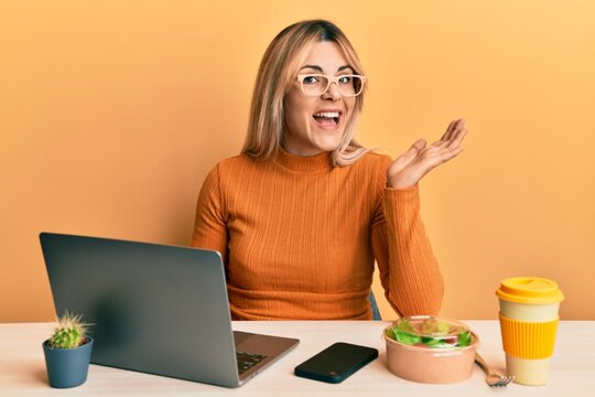Young caucasian woman working at the office wearing glasses celebrating achievement with happy smile and winner expression with raised hand