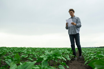 young guy farmer looks at the report and inspects the field. The farmer's son inspects the land with reports in his hands