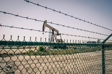 Vintage oil field with pump jack behind fence
