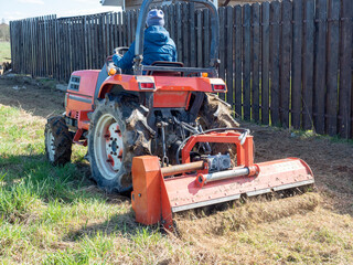 The man sits in a small tractor and drives through the field mulching grass. Land cultivation,...