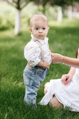 Cute little baby boy takes the first steps on the grass in summer, on a Sunny day, playing with a cat. Selective focus, space for text