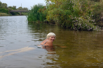 Woman is posing in the river water in cloudy day.