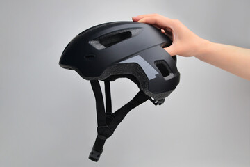 Hand holding bicycle safety helmet for mountain bike or all purpose rider on grey background. This helmet is used to practice cycling. Bike helmet. Black bicycle helmet.  - Powered by Adobe