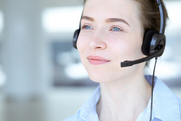 Beautiful female specialist with headphones helping customers online and smiling charmingly in modern call center office. Business people concept