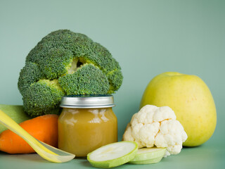Glass jar with natural baby food on the table: vegetable puree with zucchini, broccoli, cauliflower; selective focus