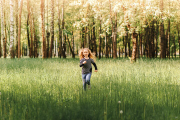 Little girl cheerfully runs on the grass in the park in the summer