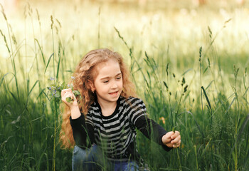 A little girl with curly hair collects flowers in the park in the summer