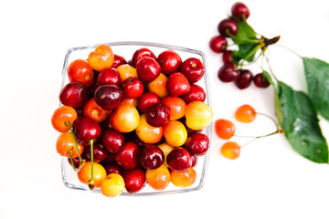 Ripe red and yellow cherries in a glass cup. Juicy cherry with leaves on a white background.