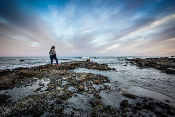 mujer caminando con olas en la playa al atardecer