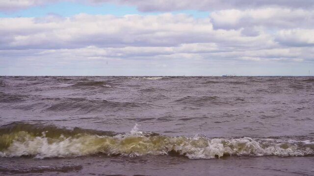 Sea coast with waves in cloudy weather close-up. Waves on the Gulf of Finland in St. Petersburg. 4K video.