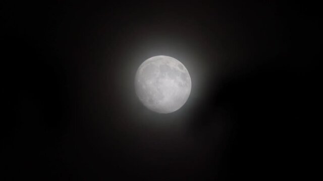 Full glowing mooon in cloudy night with slowly moving light clouds.