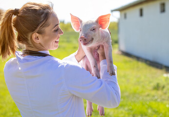 Woman vet holding adorable piglet over shoulder smiling on farm.