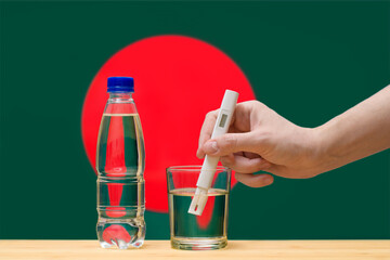 A hand with a water tester makes a measurement in a glass of clear water against the background of...