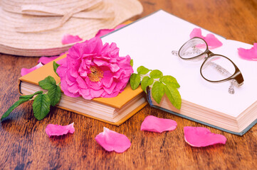 Open book, glasses for reading and rosehip flower petals on a wooden table