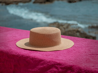 Fototapeta na wymiar Women's beach hat placed on a rock wall next to the waves of cabo de palos (la manga, Murcia). Vintage image, fashion lifestyle and exotic style. Essence of summer and good weather.