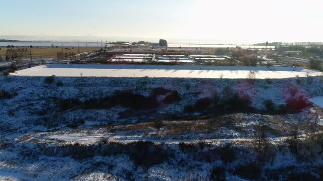 Snowy hills and rural road near contemporary waste water treatment plant with pools and equipment on winter day upper view