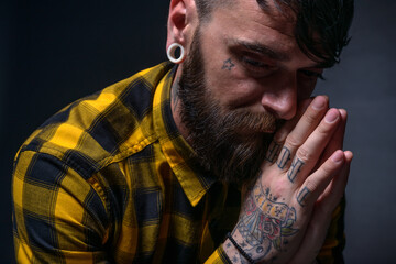 Close up portrait of a bearded man with tattoos on his hands and neck wearing yellow black shirt.