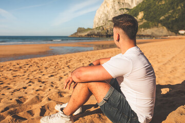 Fototapeta na wymiar Young caucasian man sitting on the sand of a basque beach.