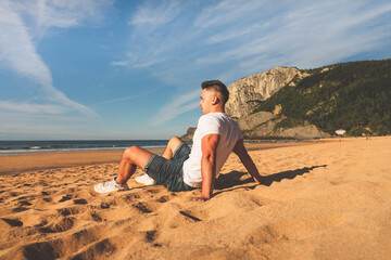 Fototapeta na wymiar Young caucasian man sitting on the sand of a basque beach.