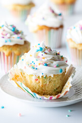 Frosted confetti cupcake unwrapped exposing inside of the cupcake.