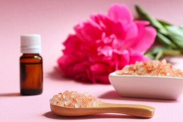 Beauty and spa concept. Pink himalayan salt close-up on a wooden spoon, essential oil and peony flower in the background. Selective focus - obrazy, fototapety, plakaty