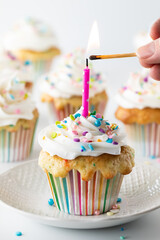 Hand lighting a candle on a frosted confetti cupcake for a birthday celebration.