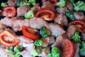 Pieces of raw meat with broccoli and tomato on a baking sheet. Cooking meat with vegetables