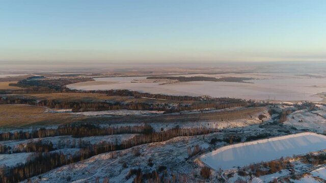 Modern waste water treatment plant on snowy land among fields and bare trees against large lake in winter aerial panorama
