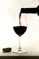 Close-up of a tall glass and bottle of red wine with light background