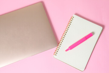 computadora junto con una libreta y un marcatextos, en fondo uniforme con todo rosa pastel