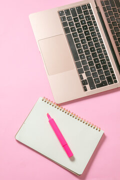 computadora junto con una libreta y un marcatextos, en fondo uniforme con todo rosa pastel