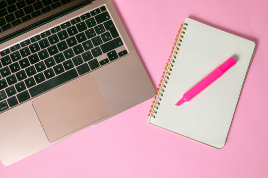 computadora junto con una libreta y un marcatextos, en fondo uniforme con todo rosa pastel