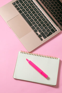 computadora junto con una libreta y un marcatextos, en fondo uniforme con todo rosa pastel