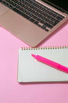 computadora junto con una libreta y un marcatextos, en fondo uniforme con todo rosa pastel