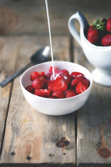 A stream of milk is poured into a bowl of strawberries. Cooking strawberry dessert with milk.